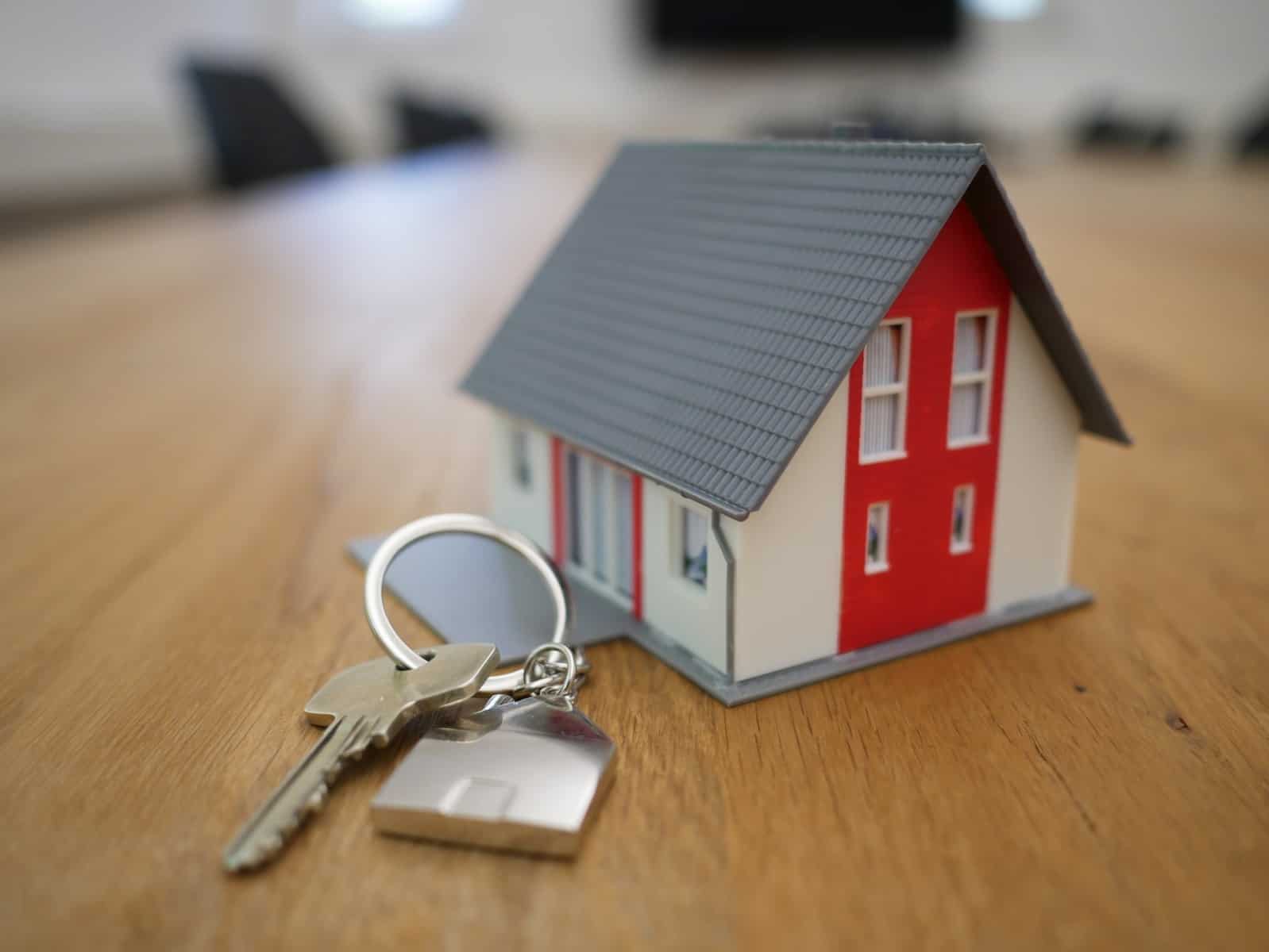 מיניאטורה של בית עץ לבן ואדום על שולחן חום כאשר מפתחות לבית לצידו